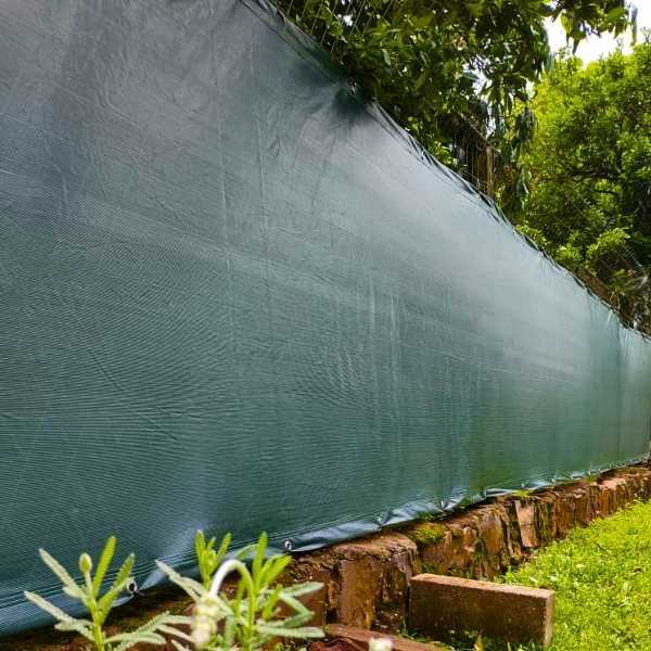 tela de privacidade verde instalada em uma cerca com plantas por perto
