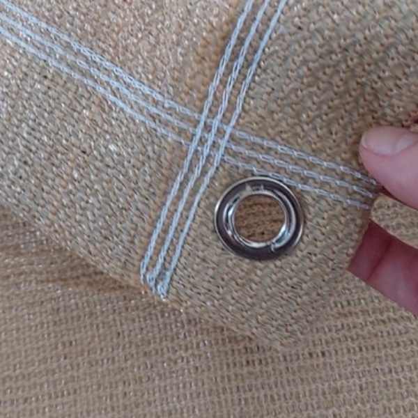 Detalhe da tela shade bege com ilhós metálico e costura reforçada, acabamento resistente que facilita a fixação e aumenta a durabilidade da cobertura.