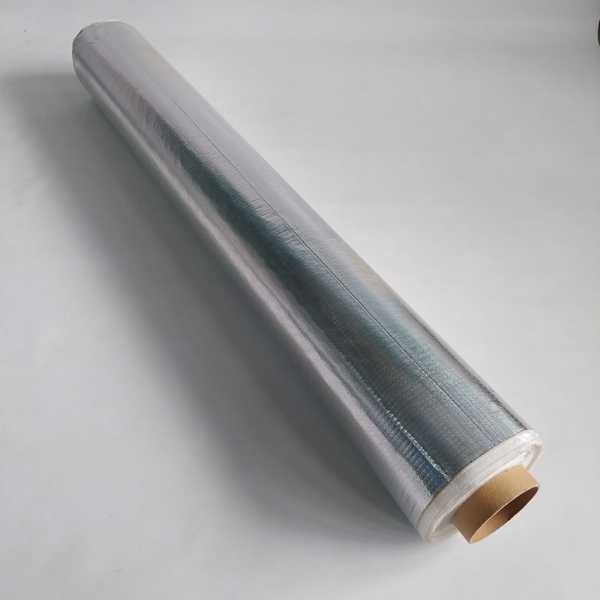 Rolo completo de manta aluminizada sobre superfície branca, com aparência metálica brilhante e tubo interno de papelão.